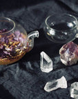 Teapot with a glass cup and crystals on a dark fabric background