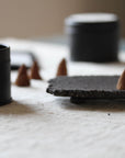 Incense cones and a black container on a textured surface with a blurred background