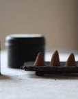 Incense cones on a holder with black containers in the background