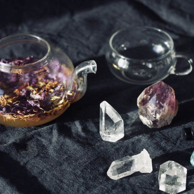 Teapot with a glass cup and crystals on a dark fabric background