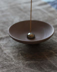 Incense stick in a small brown dish on a textured surface